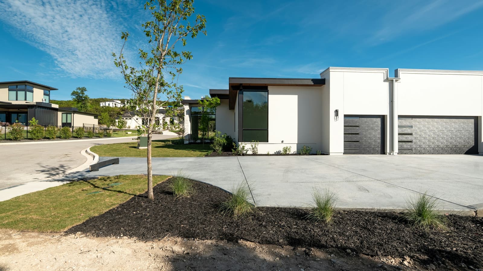 Modern single-story home with two-car garage, landscaped bed and bright blue sky